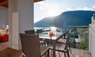 A cozy terrace with a table and chairs. In the background is a beautiful view of mountains and water at sunset.