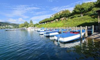 A quiet lake with small boats at the dock. In the background, green hills and a blue sky can be seen.