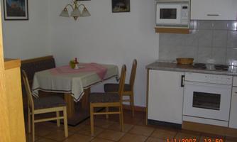 A simple kitchen with a dining table and chairs. The walls are decorated with pictures and the furnishings are functional.