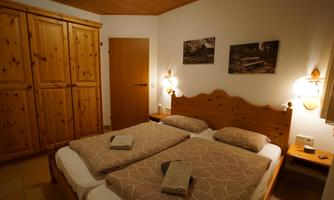 A cozy bedroom with two beds and wooden furniture. The walls are decorated with pictures and the atmosphere is inviting.