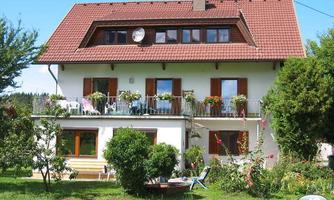 A beautiful house with a red roof and many windows. The garden has green plants and flowers.