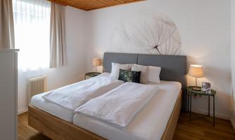 A modern bedroom with a double bed and two nightstands. Soft colors and plenty of daylight create an inviting atmosphere.