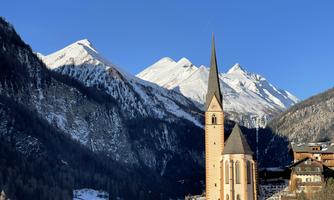 A picturesque church with a tall tower, surrounded by snow-covered mountains. The clear sky gives the landscape a special atmosphere.