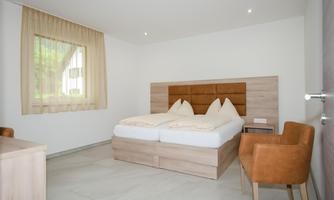 A cozy bedroom with a double bed and modern furniture. There is a window with curtains and a small desk.