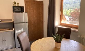 A bright, inviting kitchen with a round wooden table and two chairs. Through the window, there is a beautiful view of the mountains and nature.