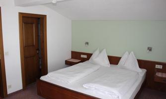 A cozy bedroom with a double bed and two pillows. The walls are painted light and there is a wooden door as well as nightstands.