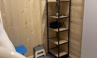 A cozy room with wooden walls and a black shelf. The shelf has several shelves and is next to a white cabinet.