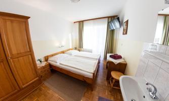A cozy room with two beds, wooden wardrobe, and window with curtains. The room also contains a sink and a table.