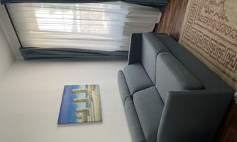 A cozy living room with a gray sofa and a rug. On the wall hangs a picture of a landscape, and the windows are decorated with blue curtains.