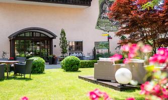 A beautiful garden with modern seating furniture and colorful flowers. In the background, there is an inviting building with lovely details.