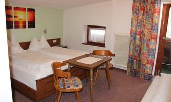 A cozy room with two beds and a table.  
Colorful curtains and a pretty wall painting create an inviting atmosphere.