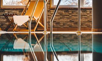 A swimming pool with shiny water and a staircase. In the background are windows with views of snow-covered landscapes and a comfortable lounge chair.