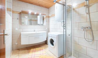 A modern bathroom with a shower, a sink, and a washing machine. The walls are brightly tiled, and there is a large mirror.
