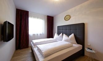A modern bedroom with a large double bed and two pillows. The room has a television and a window looking out onto daylight.