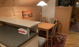 A cozy kitchen with wood paneling and a dining table. A TV is visible in the background.
