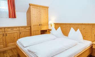 A cozy bedroom with a wooden wardrobe and two beds. The walls are bright and there is a warm atmosphere.