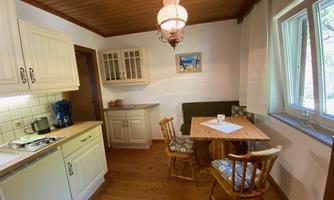 A bright kitchen with wood paneling and a small dining table. There is a kettle and some kitchen utensils visible.