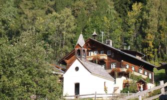 A traditional house in the midst of a green landscape. The architecture is rustic with a small church tower and surrounded by trees.