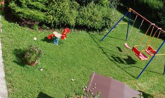 A beautiful garden with green grass and colorful play equipment. In the background, there is a swing and cozy seating options.