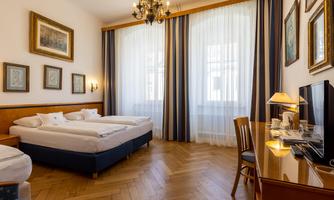 A bright room with two beds and a desk. Large windows let in plenty of light, and there are decorative pictures on the walls.