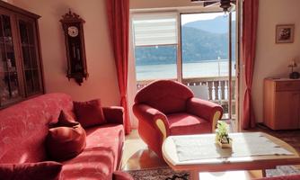 A cozy living room with a red sofa and armchair. Large windows offer a view of the lake and the mountains.