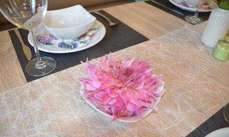 A decorative pink flower on a table. Elegant table settings and dishes accompany it.