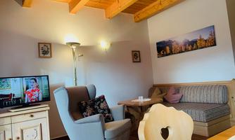 A cozy living space with a television, an armchair, and a couch. The wooden beam ceiling gives the room a warm atmosphere.