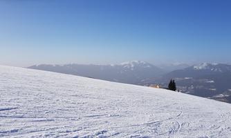 A snow-covered area under a clear blue sky. In the background, the mountains can be seen.