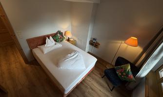 A cozy room with a double bed, a chair, and a lamp. The warm colors and the wooden floor create an inviting atmosphere.