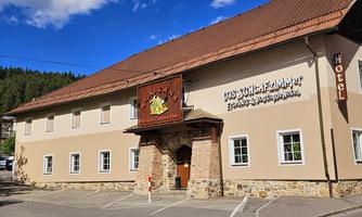 A cozy hotel building with a striking facade and a traditional sign. It is located in a quiet setting with trees in the background.