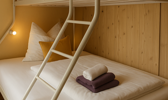 A cozy sleeping setup with a bunk bed in a warm, wood-paneled room. The bedding is neatly folded and there is soft lighting for a relaxed atmosphere.