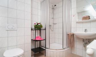 A modern bathroom with a shower, a sink, and a toilet. The walls are tiled with white tiles and there are some decorative elements.