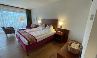 A modern bedroom with a double bed and a cozy armchair. Large windows provide plenty of light and a view outside.