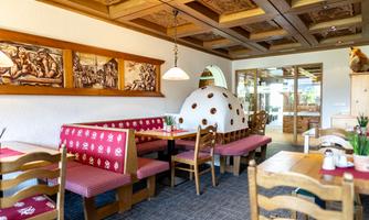 A cozy room with traditional furnishings. There are wooden chairs, red striped benches, and artistic wall murals.
