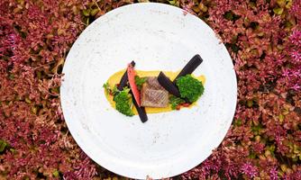 An elegant dish on a white plate, surrounded by colorful vegetables. The presentation is appealing and showcases fresh ingredients.