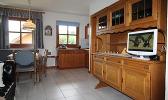 A cozy living room with a wooden cabinet and a television. The room has large windows and a dining area with a table and chairs.
