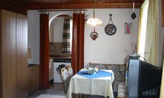 A cozy living room with a dining table and chairs. The walls are painted in light colors, and there is a small kitchen in the background.