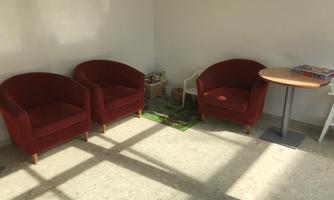 Cozy, red armchairs are positioned in a bright room. A small table with games is nearby.