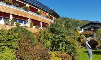 A beautiful garden with lush greenery and various plants. In the background, modern buildings and a clear blue sky can be seen.