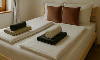 A cozy bedroom with a double bed and decorative pillows. Neatly folded towels in various colors are placed on the bed.