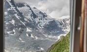 A view from a window onto majestic mountains with snow and clouds. The landscape showcases an impressive alpine scenery.