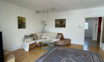 A bright living room with a large rug and a cozy couch. Some pictures hang on the wall and there is a lamp in the room.