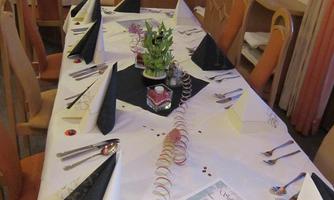 A festively set table in a restaurant with black and white napkins. In the center stands a decorative plant, surrounded by cutlery and a menu.