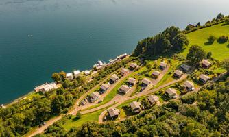 A picturesque landscape with a group of vacation cottages by the shore of a tranquil lake. Surrounded by lush greenery and trees, the place offers a relaxing atmosphere.
