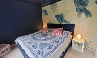 A modern bedroom with a large bed and a blue wall. The decoration includes striped cushions and an artistic wallpaper featuring fish.