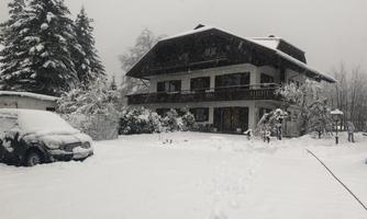 A large house in the snow with snow-covered trees and a snow-covered car. The landscape looks calm and wintry.