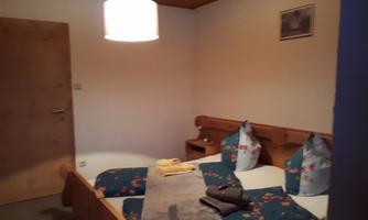 A cozy bedroom with a double bed, covered with colorful bedding. A wooden wardrobe and a bedside table complement the furnishings.
