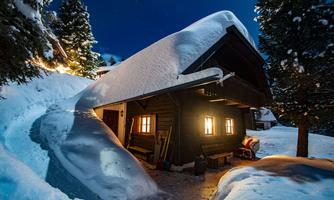 A cozy cabin in the snow at night. The garden is covered with sparkling snow, and the windows radiate warm light.
