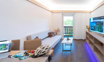 A modern living room with a comfortable sofa and a large television. A table with a laptop and a bicycle helmet showcases an active lifestyle.