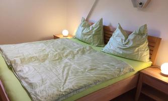 A bright bedroom with a large bed and green bedding. Two nightstands with gentle lamps complement the cozy atmosphere.